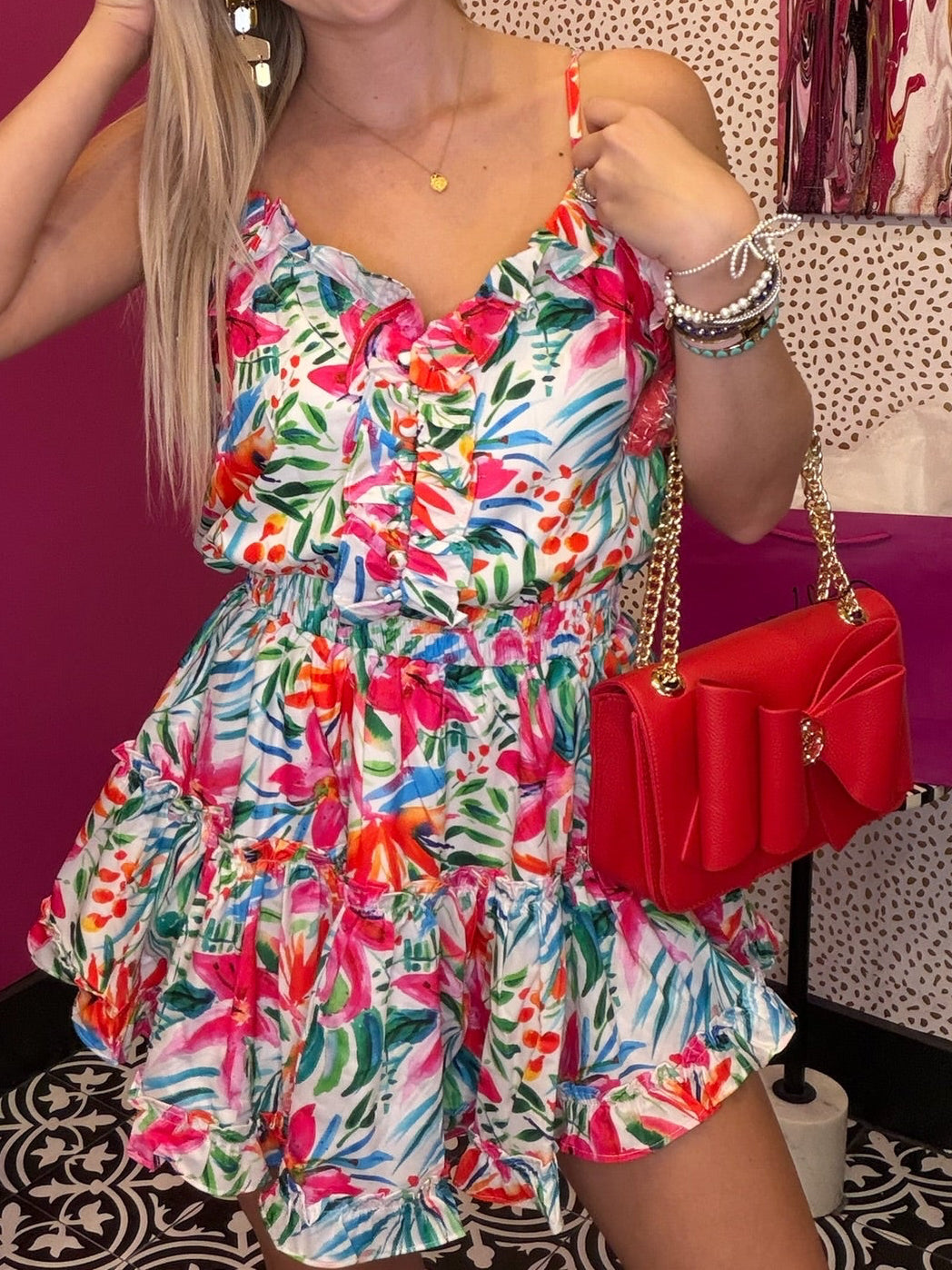 Woman in a colorful floral dress holding a red handbag in a store setting.
