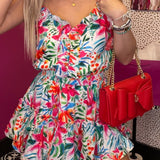 Woman in a colorful floral dress holding a red handbag in a store setting.