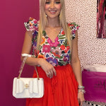 Woman in colorful top and red skirt holding a white handbag in a store setting.