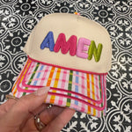 Colorful pouch with 'AMEN branding held by a hand against a patterned background
