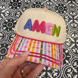 Colorful pouch with 'AMEN branding held by a hand against a patterned background
