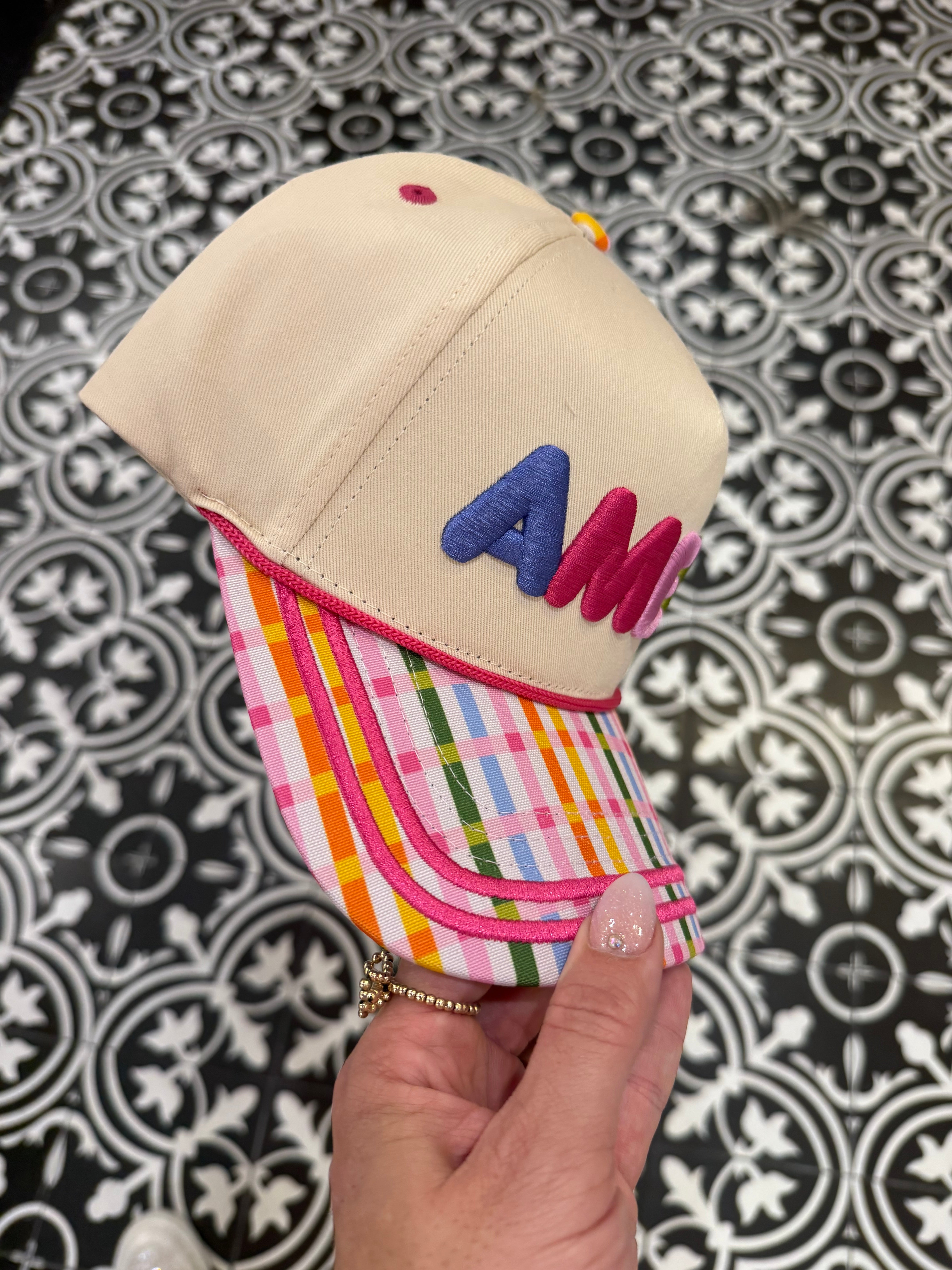Hand holding a small beige hat with colorful brim against a patterned background