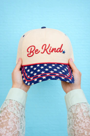 Cap with 'Be Kind' text and American flag design held against a blue background