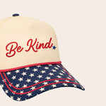 Cap with 'Be Kind' text and American flag pattern on a beige background with stars on the bill
