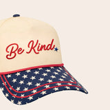 Cap with 'Be Kind' text and American flag pattern on a beige background with stars on the bill