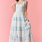 Woman wearing a long, tiered dress with blue ruffles on a pink background