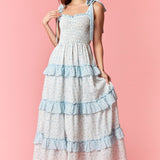 Woman wearing a long, tiered dress with blue ruffles on a pink background