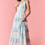 Woman wearing a layered dress with blue accents on a pink background