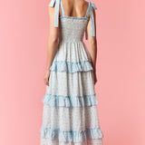 Woman wearing a light blue and white tiered dress on a pink background