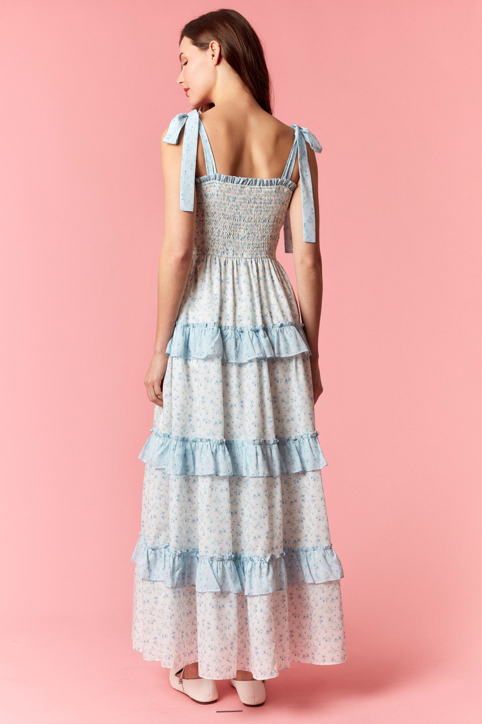 Woman wearing a light blue and white tiered dress on a pink background