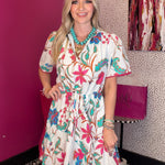 Woman in a floral dress standing in a room with a pink wall and abstract painting.