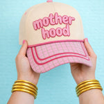 Cap with neutral crown, pink raised embroidery reading ‘Motherhood,’ pink grid print bill with contrast trim, and a front rope detail