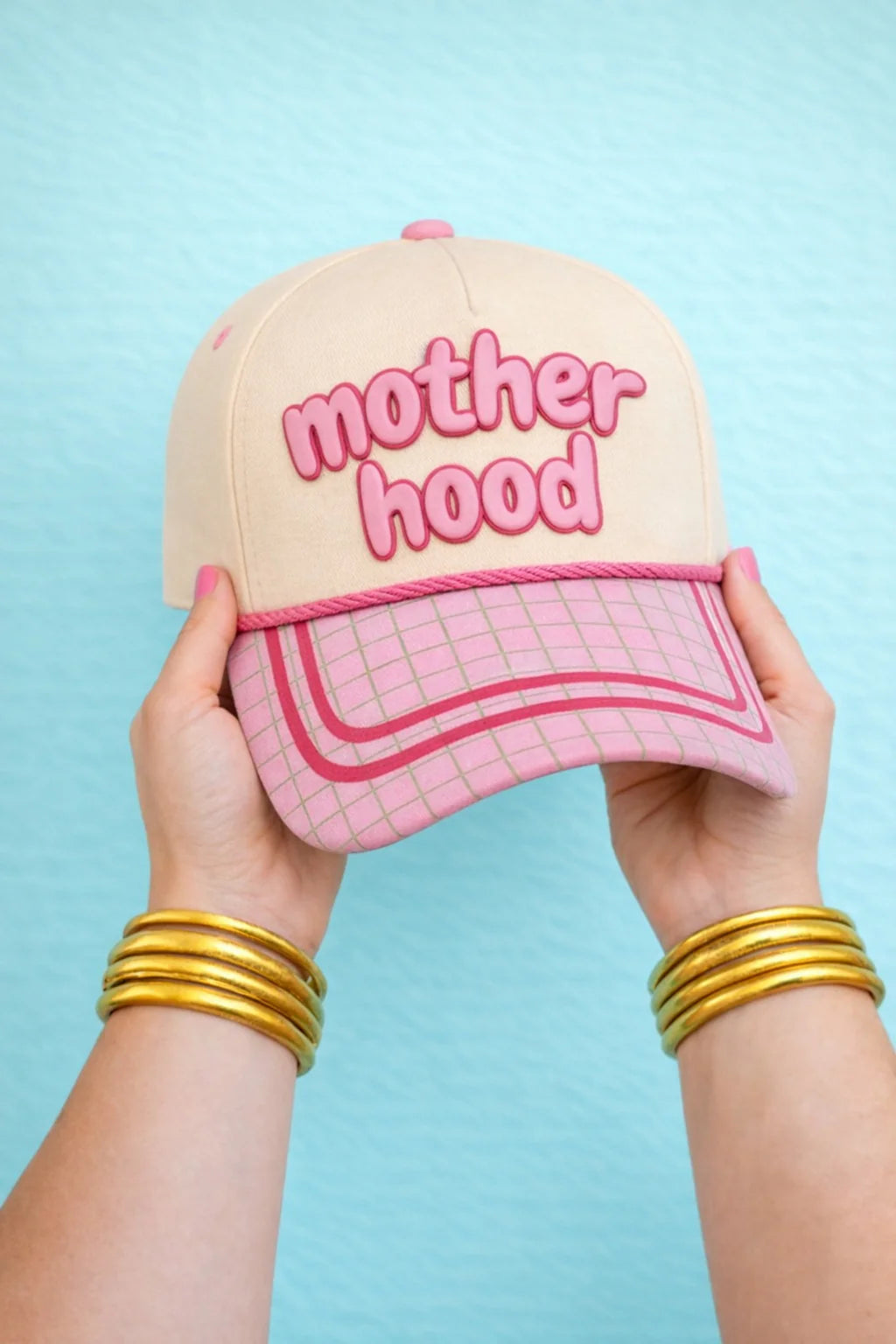 Cap with neutral crown, pink raised embroidery reading ‘Motherhood,’ pink grid print bill with contrast trim, and a front rope detail