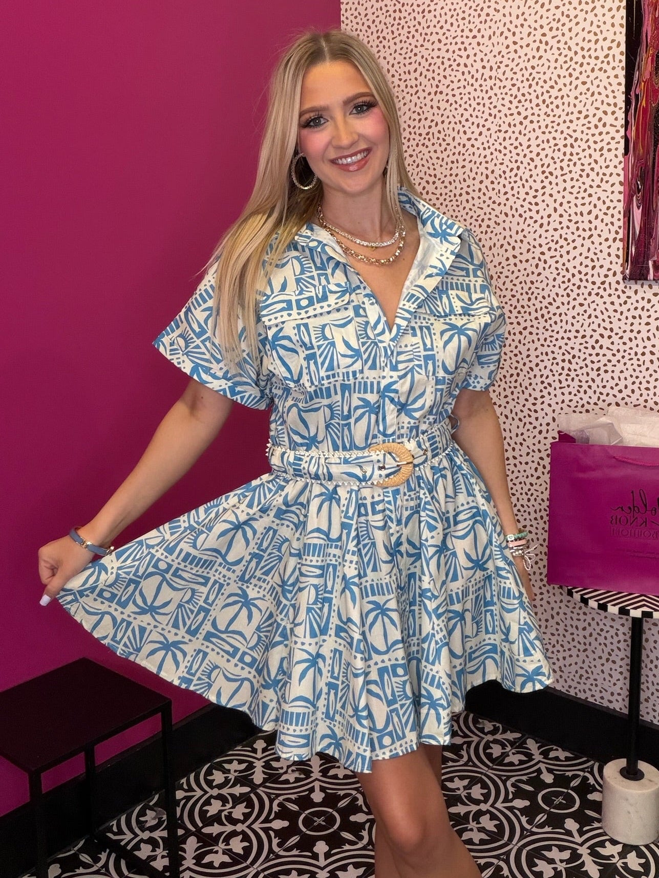 Woman in a blue and white dress posing in front of a pink wall with a polka dot pattern.