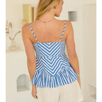 Woman wearing a blue and white striped top and white shorts in a minimal indoor setting.