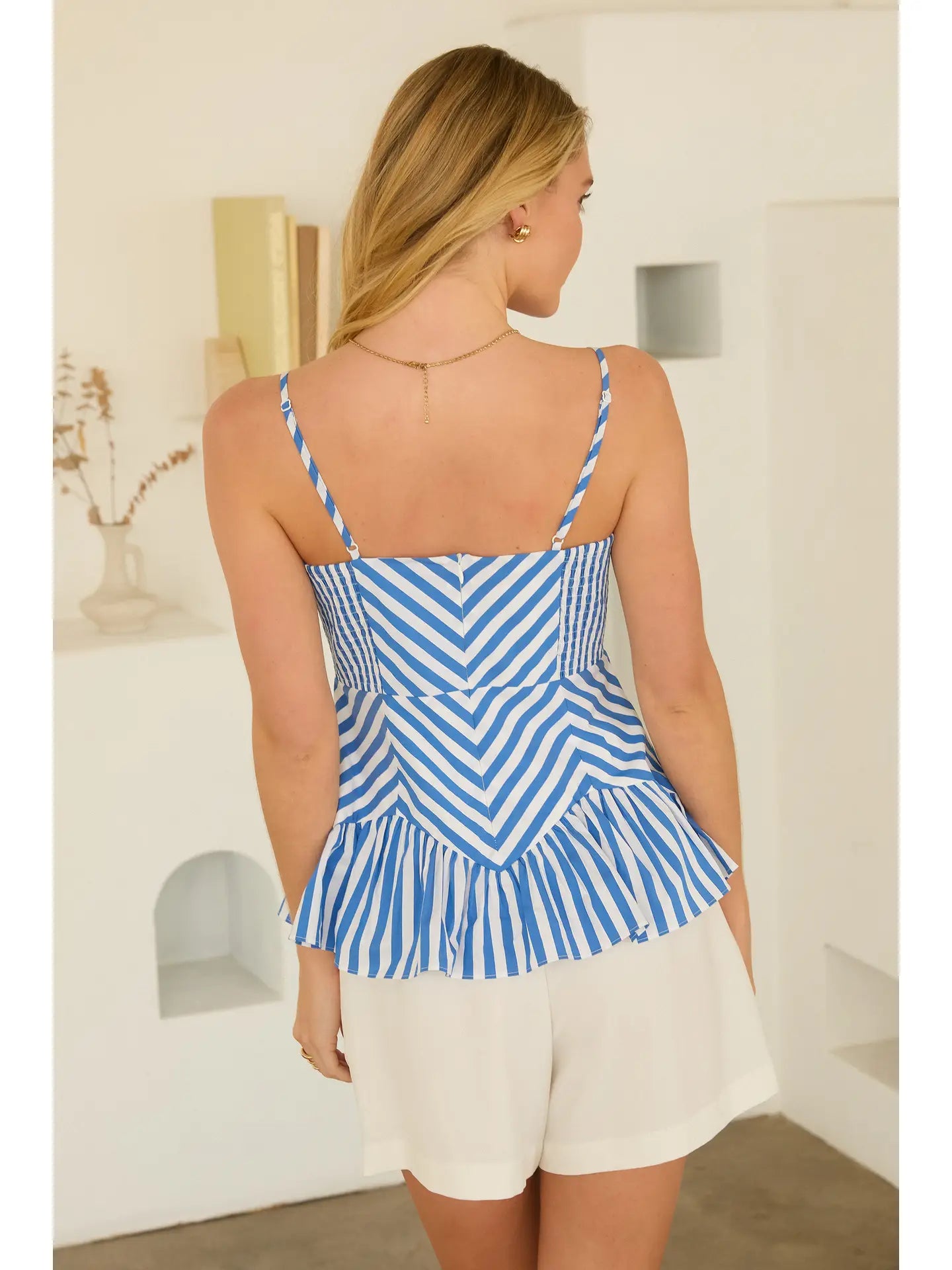 Woman wearing a blue and white striped top and white shorts in a minimal indoor setting.