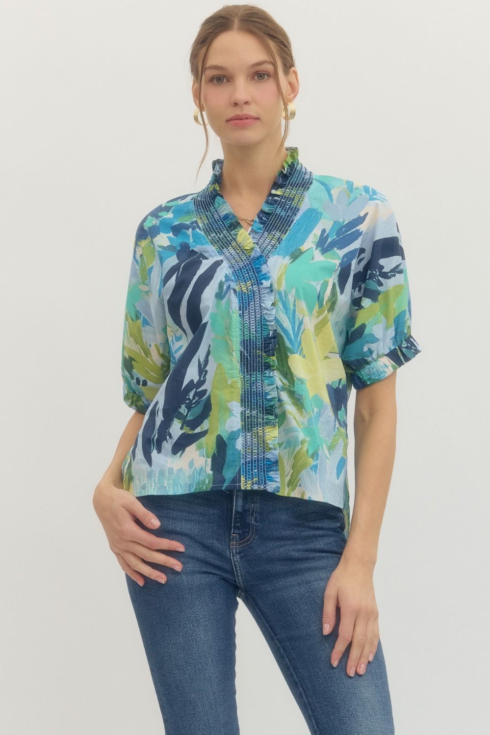 Woman wearing a colorful patterned blouse and blue jeans on a plain background