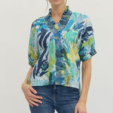 Woman wearing a colorful patterned blouse and blue jeans on a plain background