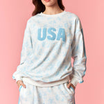 Woman wearing a 'USA' sweatshirt and shorts set on a pink background