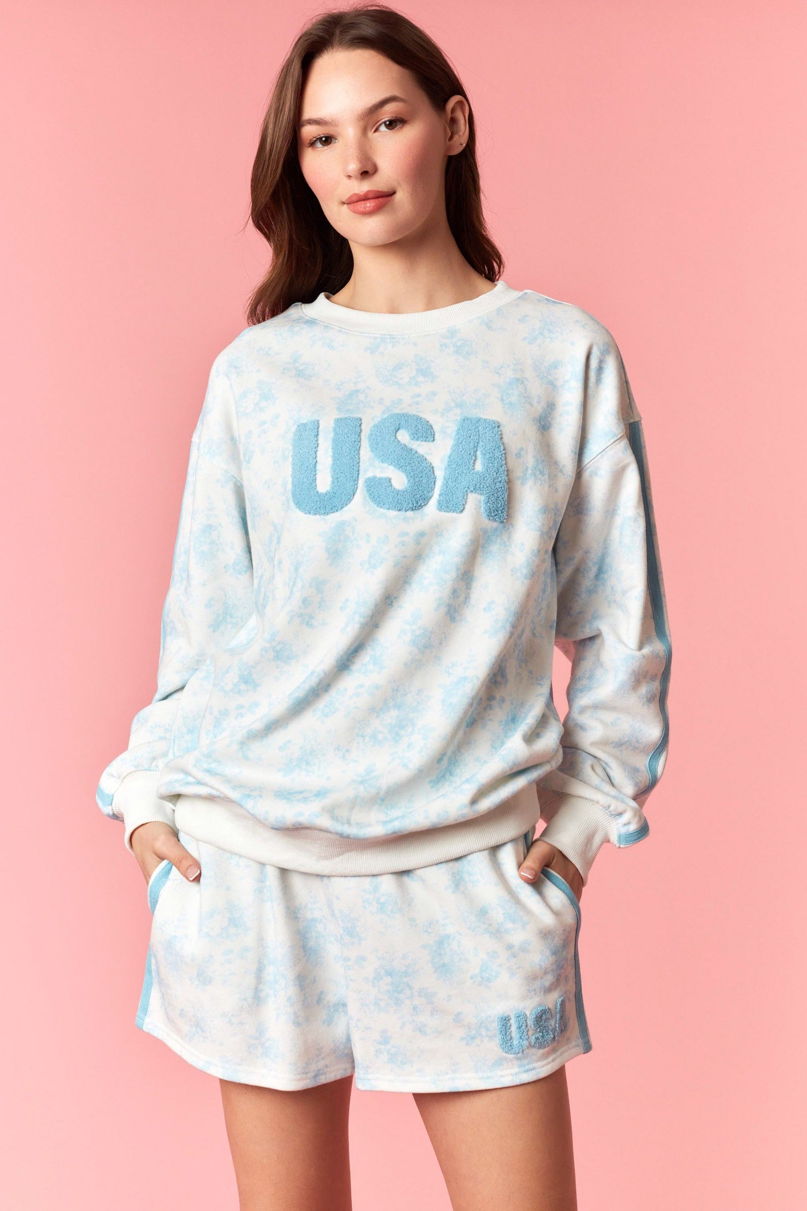 Woman wearing a 'USA' sweatshirt and shorts set on a pink background