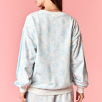 Person wearing a light blue tie-dye sweatshirt and shorts set on a pink background