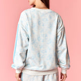 Person wearing a light blue tie-dye sweatshirt and shorts set on a pink background