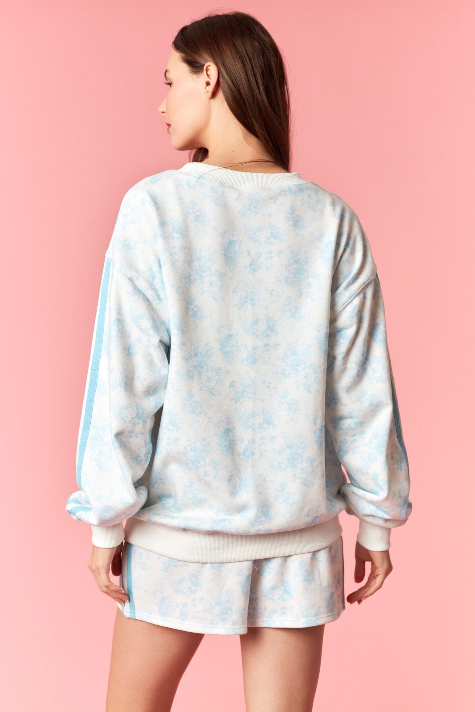 Person wearing a light blue tie-dye sweatshirt and shorts set on a pink background