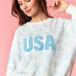 Woman wearing a white sweatshirt with blue text 'USA' against a pink background