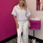 Woman in a striped shirt and white pants standing in a room with a pink wall and patterned floor.