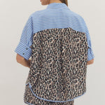 Person wearing a shirt with blue sleeves and leopard print body on a plain background