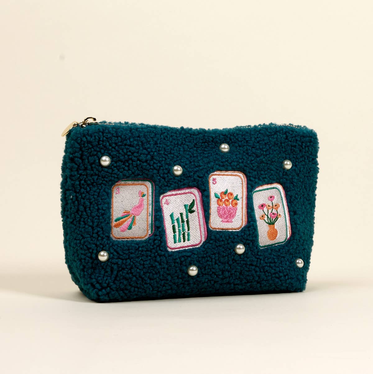 Teal pouch with embroidered designs on a beige background